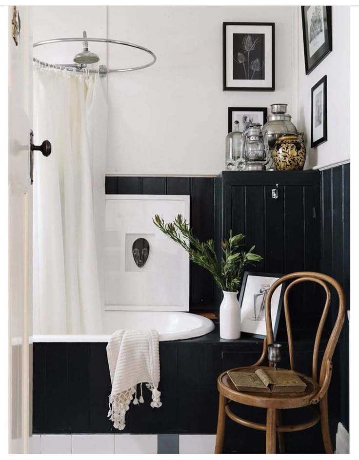 A bedroom with a bed, white and gray bedding, and a small side table with a dark metal lamp. A gallery wall of framed photos is arranged on a white brick wall.