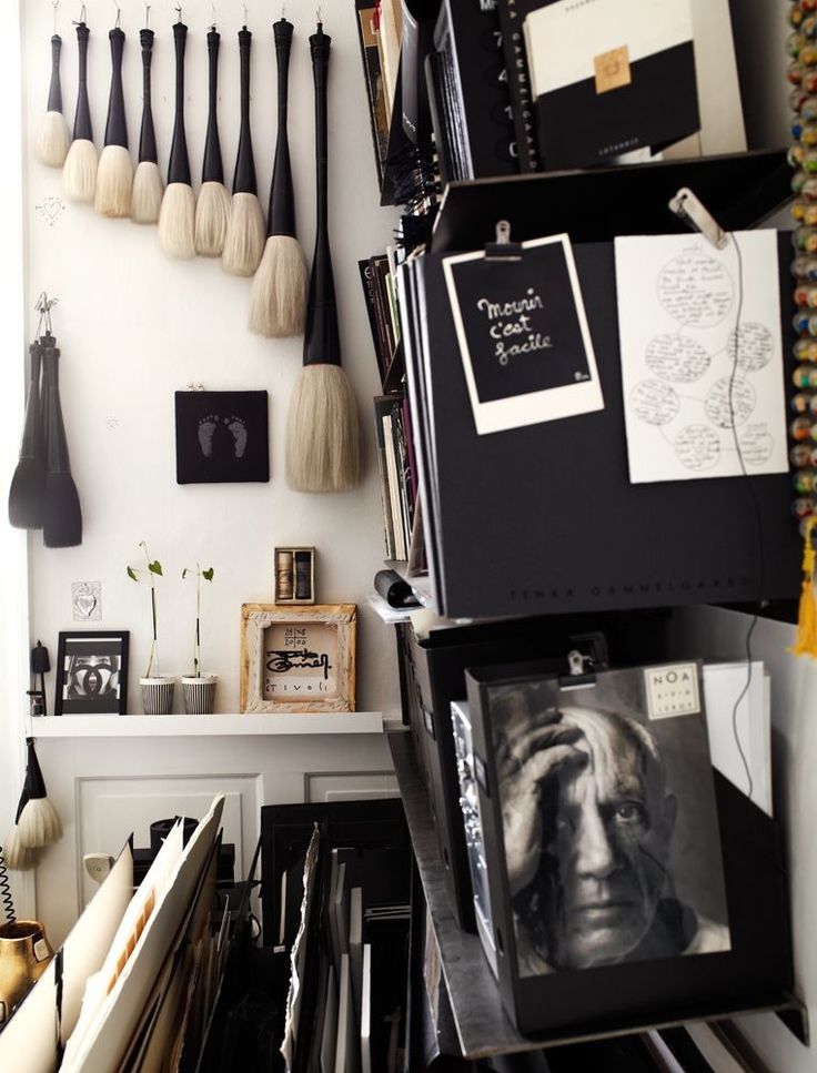 An artistic space with a wall display of large hanging paint brushes and small framed art. A black metal rack holds a black-and-white portrait of Pablo Picasso and other art supplies.