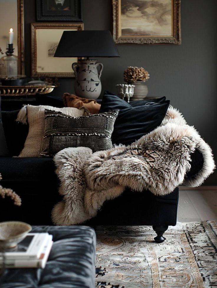 A living room with a plush couch layered with pillows and a blanket, lit by exposed bulb pendant lights hanging in front of a large window.