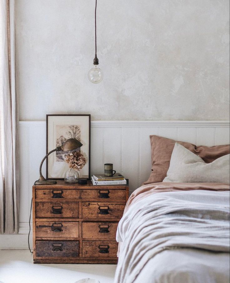 A bedroom with a unique, multi-drawer apothecary-style nightstand and a bed with neutral-toned bedding.