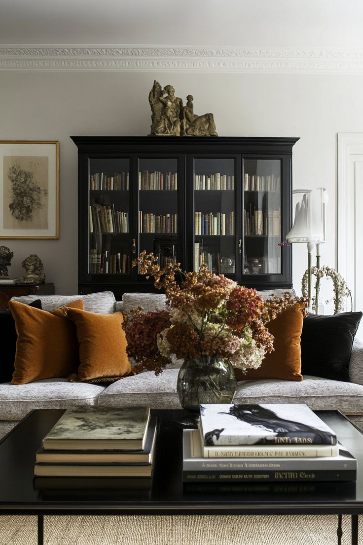 Elegant living room with black bookcase, neutral sofa, and burnt orange velvet pillows creating a warm, deep fall style.