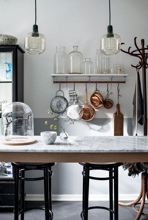 A close-up of a kitchen counter showcasing moody lighting from warm under-cabinet LEDs, highlighting a matte black fruit bowl and dark stoneware mugs.