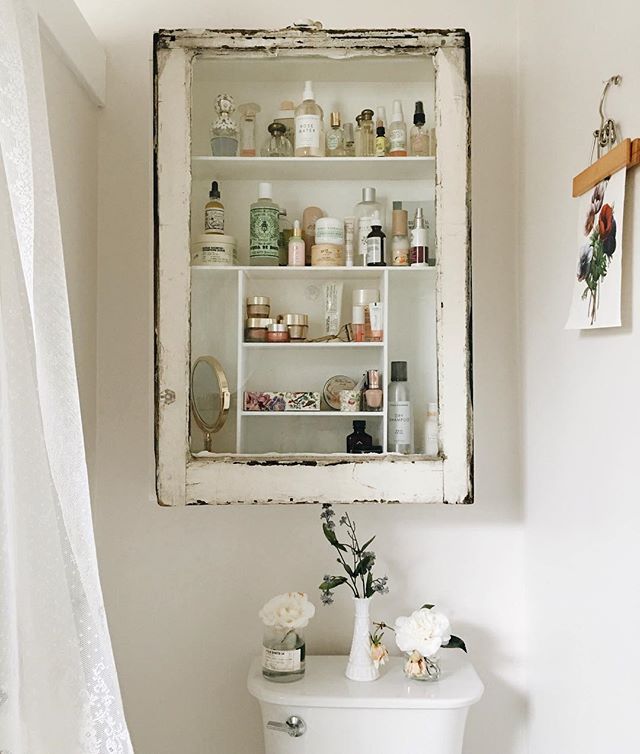 An ornate antique mirror with a weathered gold frame and a decorative carved top panel, reflecting a bright, chic bathroom space.