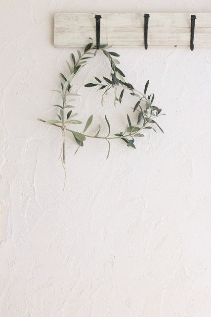 A heart shaped wreath of olive branches hanging on a peg on a whitewashed wall