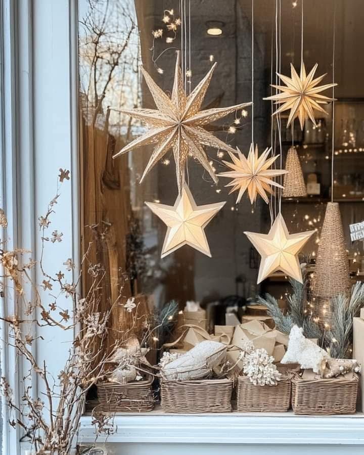 A large, white geometric paper star with an LED light hangs in a window, casting a warm, soft glow, framed by subtle white curtains.