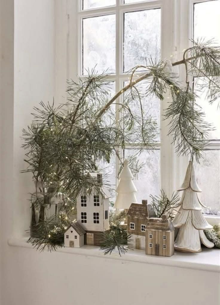 A serene winter living room featuring a cream-colored knit throw, a wooden tray with pine sprigs and candles, and a subtle glow from white lights in the background.