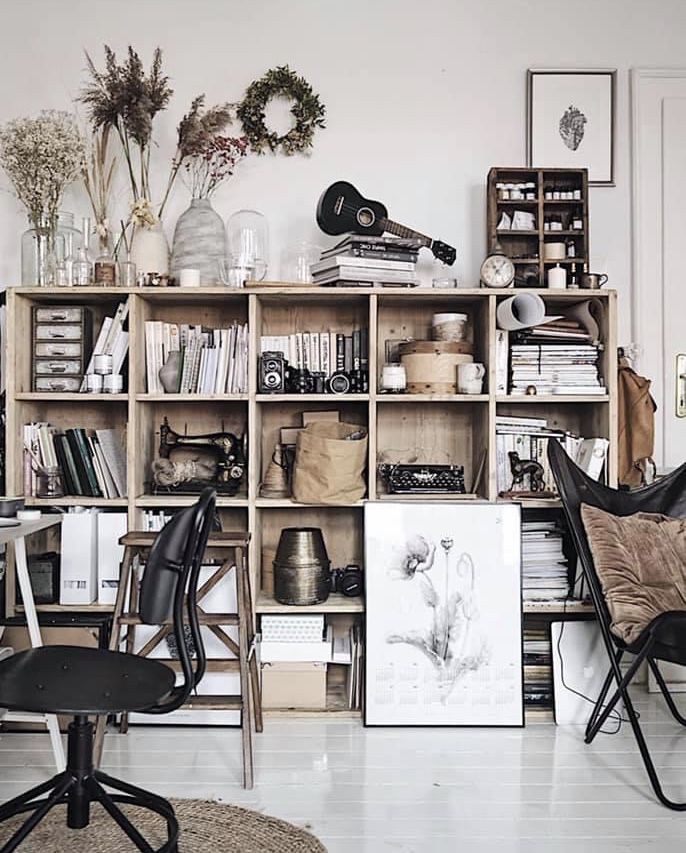 A quiet reading nook in a home office featuring a rattan armchair, a large fiddle-leaf fig in a terracotta pot, and a stack of vintage books on the floor.