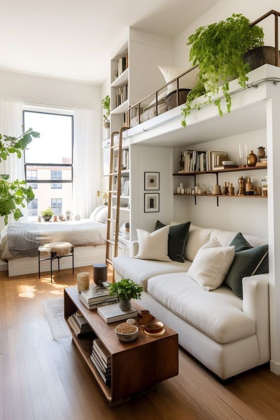 A tall, black metal open-backed bookshelf used as a room divider in a modern loft. The shelves are curated with a mix of vintage books and upright Snake Plants, creating a semi-private 'wall' between the sleeping area and the main room.