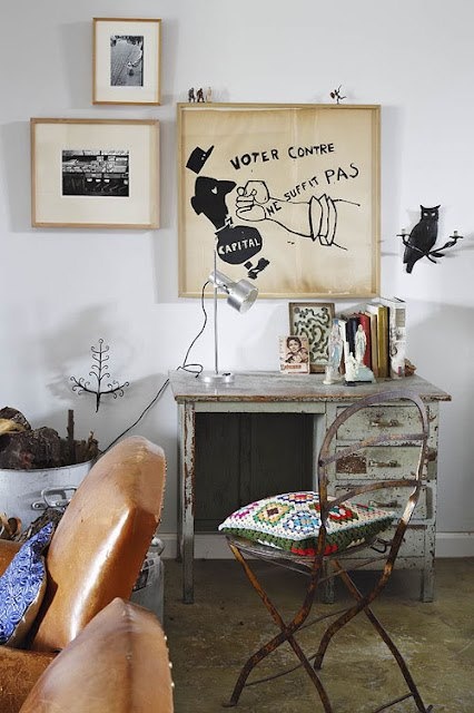 A small, elegant office nook featuring a vintage dark wood writing desk paired with a modern matte black chair. A brass task lamp sits on the desk next to a stack of linen-bound notebooks.