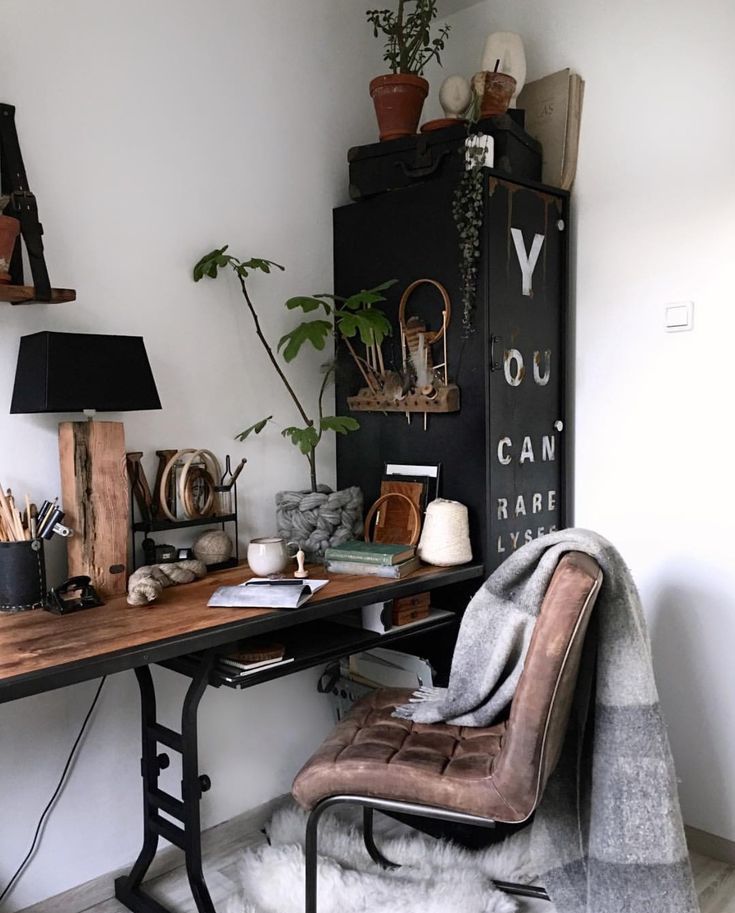 A bright, modern living room featuring a charcoal grey velvet sofa, a large circular wooden coffee table, and tall green potted plants in the corner against a white brick wall.