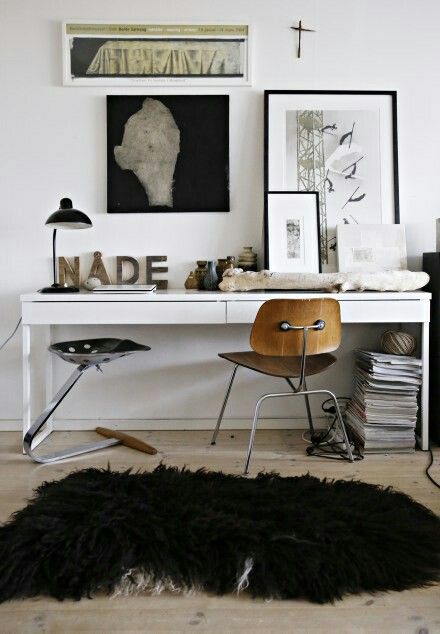 A cozy, nostalgic workspace with dark wood floor-to-ceiling bookshelves, a small antique writing desk styled with a green glass banker's lamp, and a collection of old-fashioned portrait art in mismatched gilded frames.